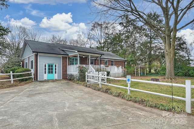 ranch-style home featuring driveway, covered porch, a fenced front yard, and brick siding