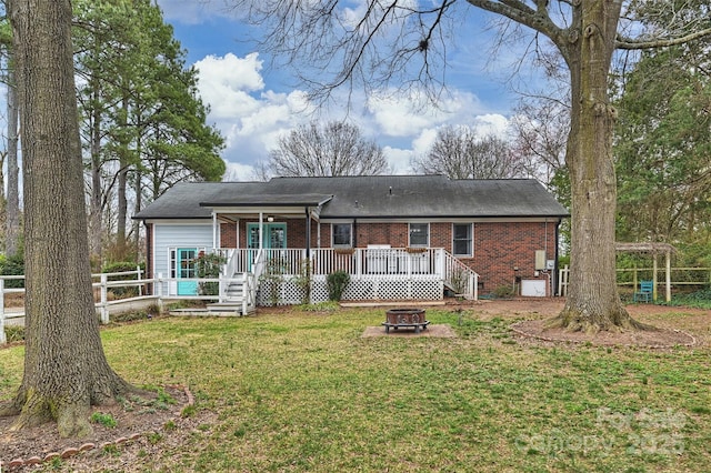 rear view of house with brick siding, a yard, a fire pit, and fence