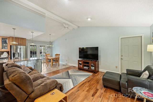 living room with lofted ceiling with beams, light wood-type flooring, baseboards, and a ceiling fan