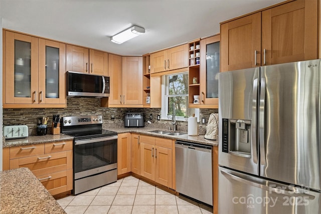 kitchen with light tile patterned floors, stainless steel appliances, decorative backsplash, a sink, and light stone countertops