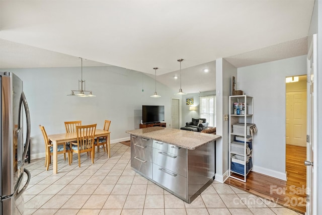 kitchen with light tile patterned floors, baseboards, freestanding refrigerator, and light stone countertops