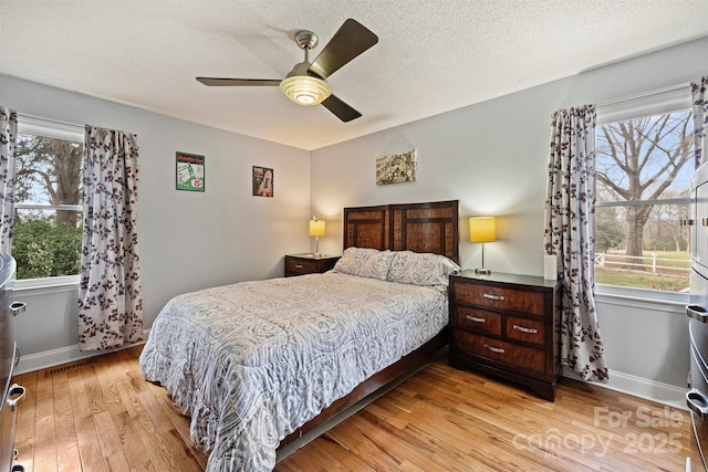 bedroom with light wood-type flooring, multiple windows, a textured ceiling, and baseboards