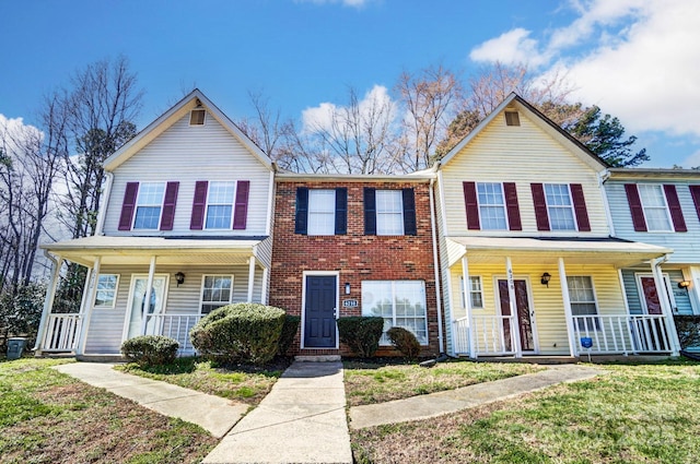 view of property with a porch, brick siding, and a front lawn