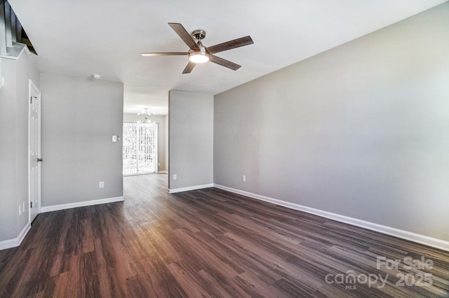 empty room featuring dark wood-type flooring, baseboards, and ceiling fan with notable chandelier