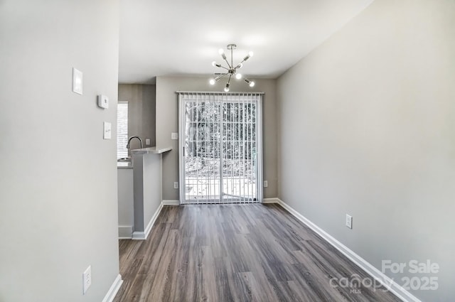 unfurnished dining area with a notable chandelier, dark wood-type flooring, a wealth of natural light, and baseboards