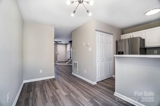 kitchen with dark wood-style floors, stainless steel fridge, white cabinetry, and baseboards