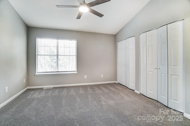 unfurnished bedroom featuring baseboards, ceiling fan, vaulted ceiling, carpet floors, and two closets