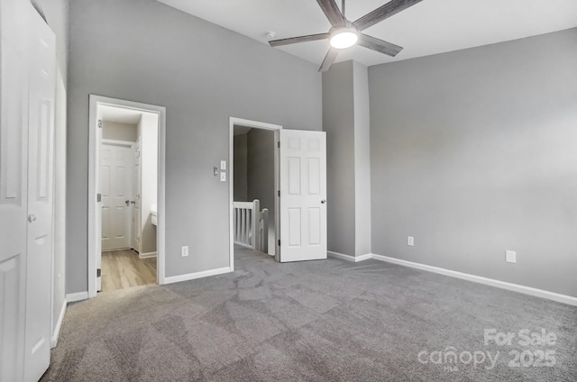 unfurnished bedroom featuring ensuite bathroom, carpet flooring, a towering ceiling, and baseboards