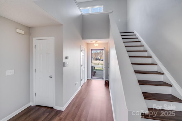 foyer entrance featuring dark wood-style floors, stairway, baseboards, and a towering ceiling