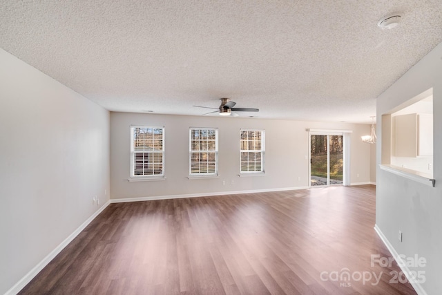 unfurnished living room featuring ceiling fan with notable chandelier, wood finished floors, baseboards, and a textured ceiling