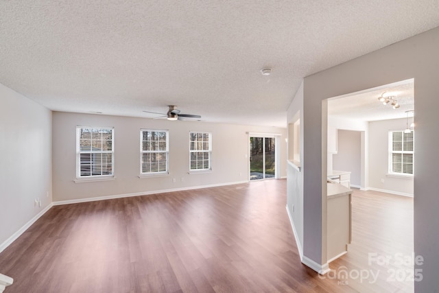 unfurnished living room featuring ceiling fan, wood finished floors, baseboards, and a textured ceiling