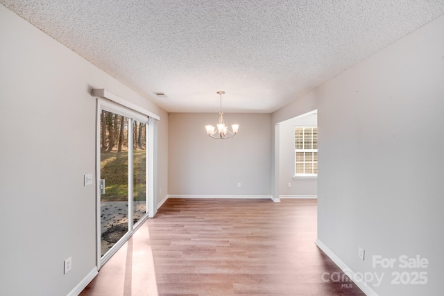 empty room featuring a notable chandelier, light wood-style floors, plenty of natural light, and a textured ceiling