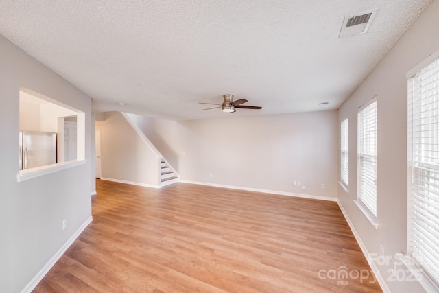 empty room with a textured ceiling, visible vents, light wood-style floors, and stairway