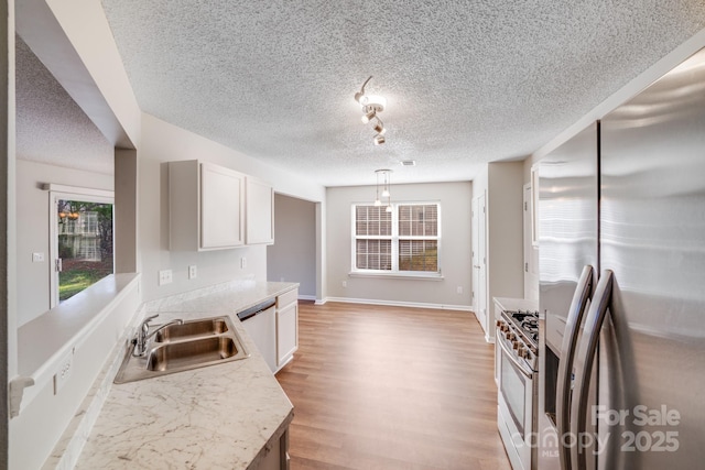 kitchen with a sink, white cabinetry, stainless steel appliances, light wood finished floors, and light countertops