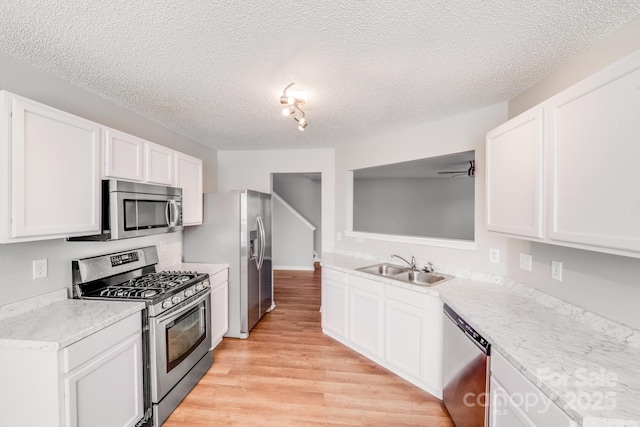 kitchen with light wood-style flooring, appliances with stainless steel finishes, a textured ceiling, white cabinetry, and a sink