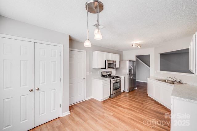 kitchen with a sink, stainless steel appliances, pendant lighting, white cabinetry, and light wood-type flooring