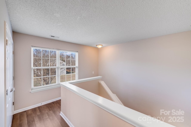 hall featuring visible vents, an upstairs landing, a textured ceiling, dark wood-style floors, and baseboards