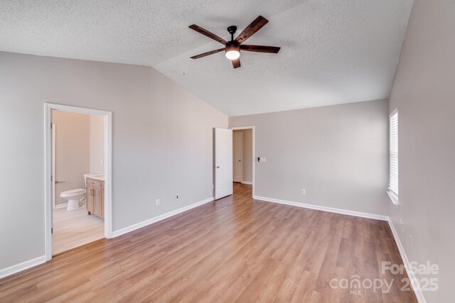 unfurnished bedroom with lofted ceiling, baseboards, light wood-type flooring, and a textured ceiling