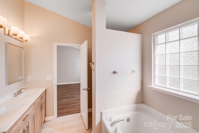 bathroom featuring a textured ceiling, double vanity, a bath, and a sink