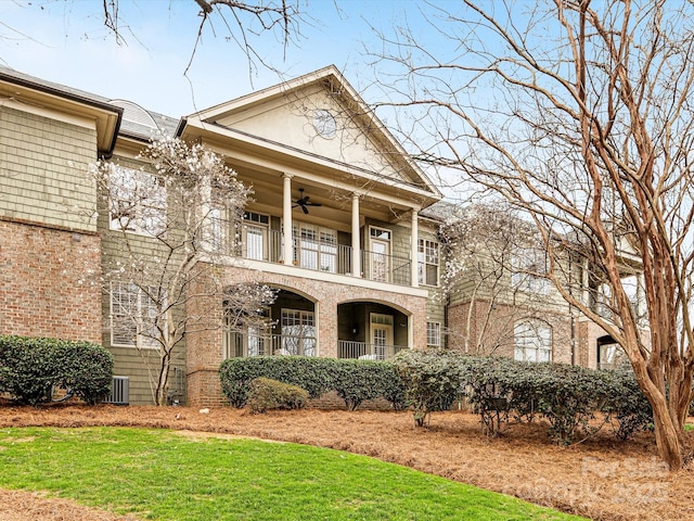 view of front of home featuring a ceiling fan, a balcony, central air condition unit, a front lawn, and brick siding