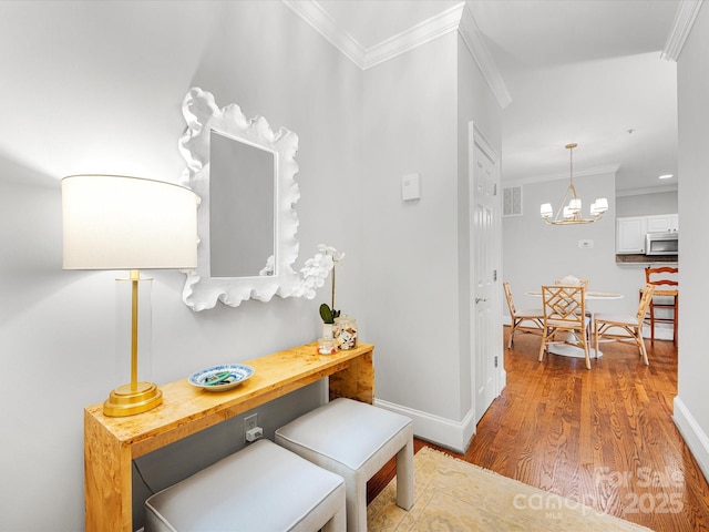 hallway featuring crown molding, visible vents, an inviting chandelier, wood finished floors, and baseboards