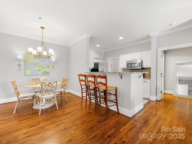 kitchen featuring stainless steel appliances, decorative backsplash, white cabinets, wood finished floors, and a kitchen bar