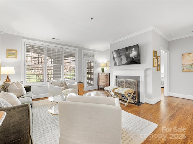 living area with a fireplace with flush hearth, crown molding, baseboards, and wood finished floors