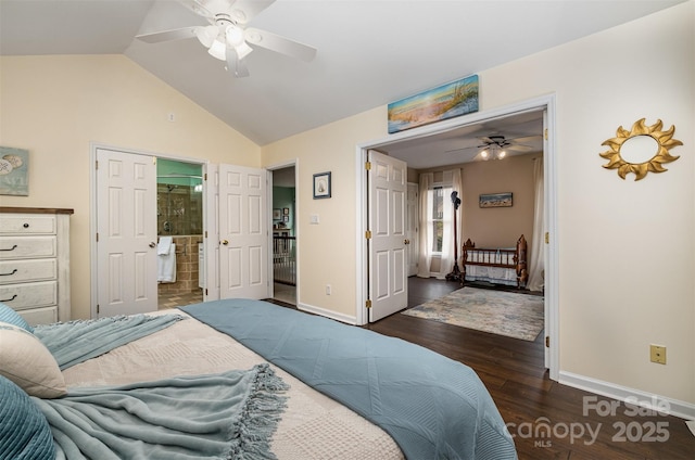bedroom featuring dark wood-type flooring, baseboards, vaulted ceiling, ensuite bath, and a ceiling fan