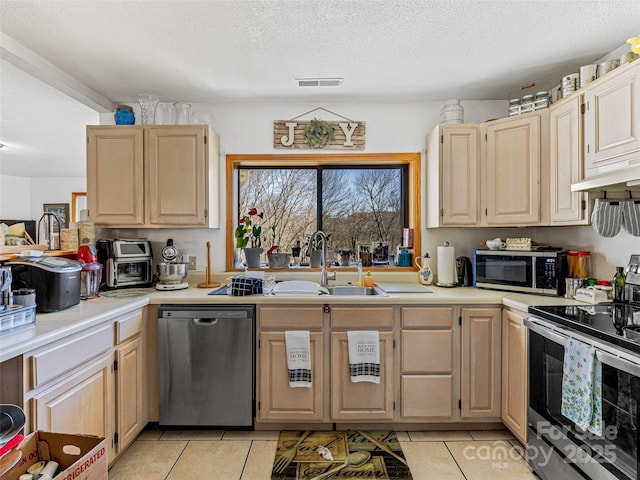 kitchen with stainless steel appliances, light countertops, a sink, and light brown cabinetry