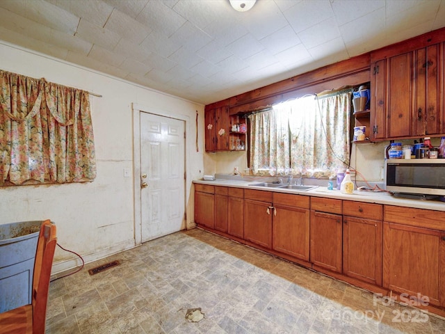 kitchen with brown cabinetry, stainless steel microwave, light countertops, open shelves, and a sink