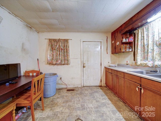 kitchen with stone finish flooring, a sink, light countertops, brown cabinets, and open shelves