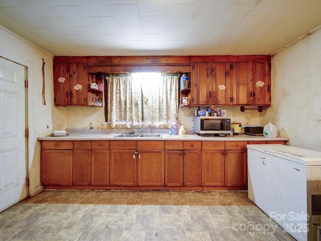 kitchen featuring brown cabinetry, stainless steel microwave, open shelves, and a sink