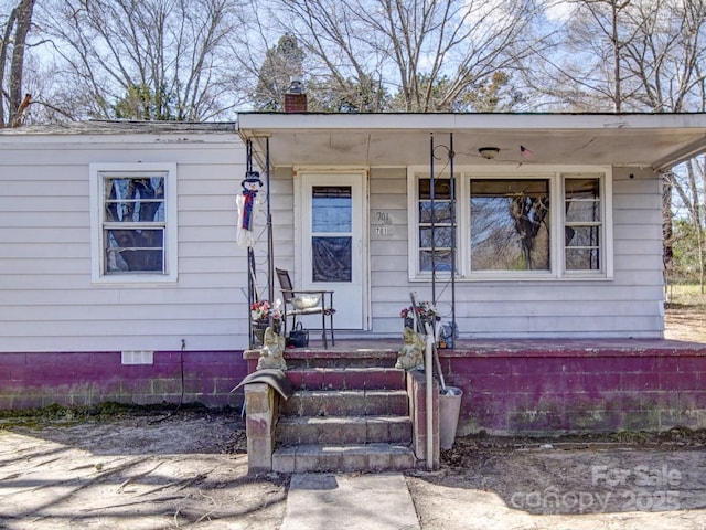 view of exterior entry with a porch and a chimney