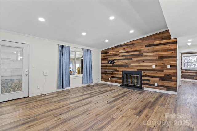 unfurnished living room featuring wood walls, a fireplace, wood finished floors, vaulted ceiling, and ornamental molding