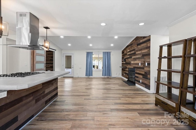 kitchen with lofted ceiling, island exhaust hood, stainless steel gas cooktop, and wood finished floors