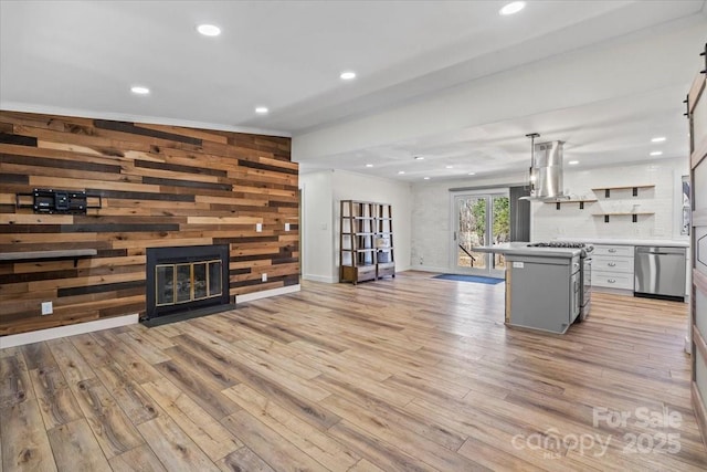 unfurnished living room with recessed lighting, wood walls, a fireplace with flush hearth, baseboards, and light wood-style floors