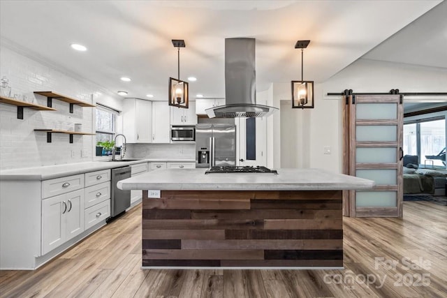 kitchen featuring a barn door, appliances with stainless steel finishes, white cabinets, a sink, and island range hood