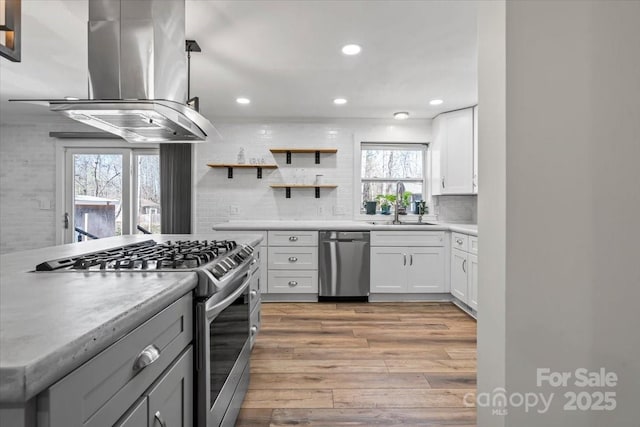 kitchen with light wood-style flooring, appliances with stainless steel finishes, island exhaust hood, light countertops, and a sink