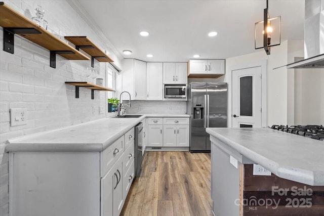 kitchen with stainless steel appliances, a sink, wall chimney range hood, decorative backsplash, and open shelves