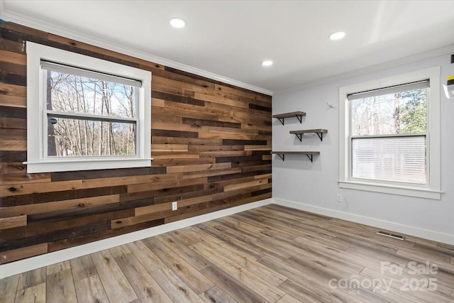 empty room with wood walls, crown molding, visible vents, and wood finished floors