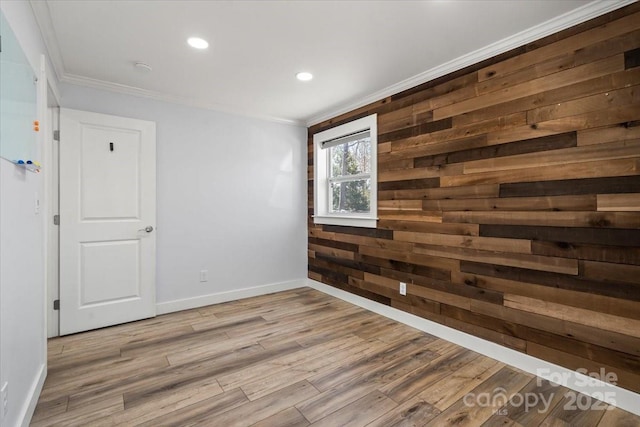 empty room featuring recessed lighting, ornamental molding, wooden walls, wood finished floors, and baseboards