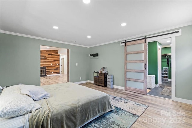 bedroom featuring recessed lighting, a spacious closet, a barn door, ornamental molding, and wood finished floors