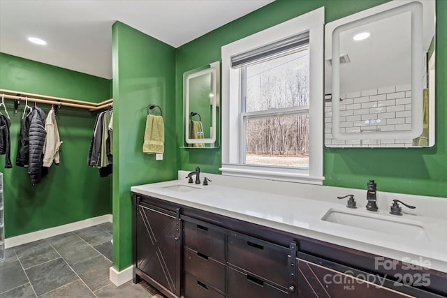 full bath featuring double vanity, baseboards, a walk in closet, and a sink