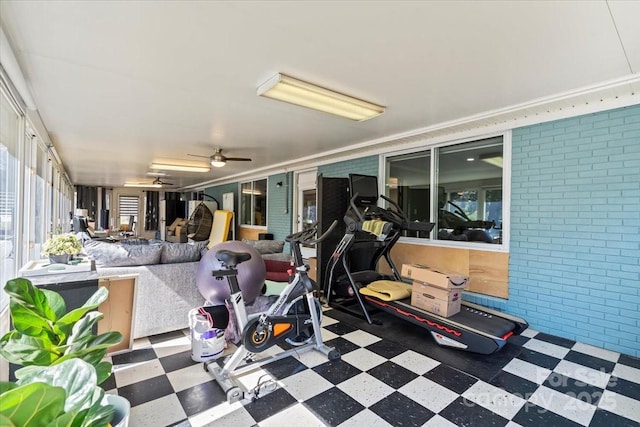 workout room with crown molding, a ceiling fan, a sunroom, brick wall, and tile patterned floors