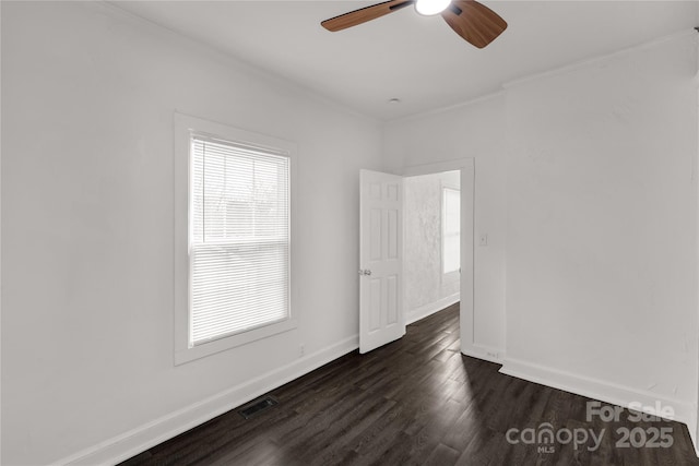 empty room with ceiling fan, visible vents, baseboards, dark wood finished floors, and crown molding