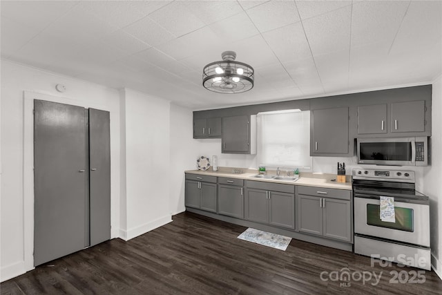 kitchen with gray cabinetry, stainless steel appliances, dark wood-style flooring, a sink, and light countertops