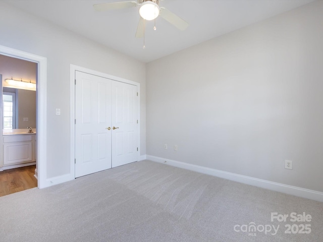 unfurnished bedroom featuring light carpet, baseboards, a ceiling fan, ensuite bath, and a closet