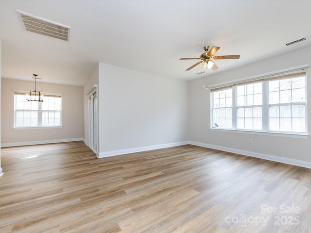 spare room with ceiling fan with notable chandelier, light wood finished floors, visible vents, and baseboards