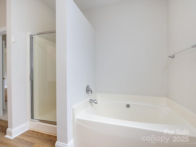 bathroom with a stall shower, a garden tub, baseboards, and wood finished floors