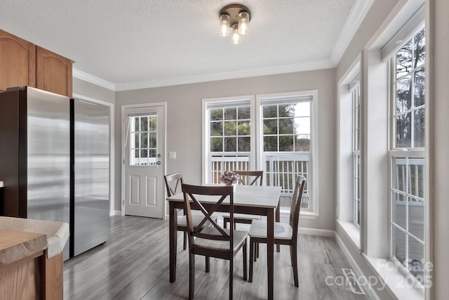 dining room featuring light wood finished floors, baseboards, ornamental molding, and a textured ceiling